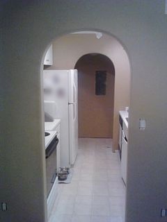 A square doorway rebuilt as a rounded archway with drywall, looking through to a kitchen