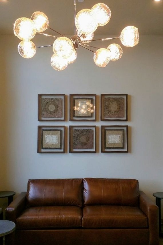 Six framed art pieces hung level in a grid above a leather sofa under a chandelier