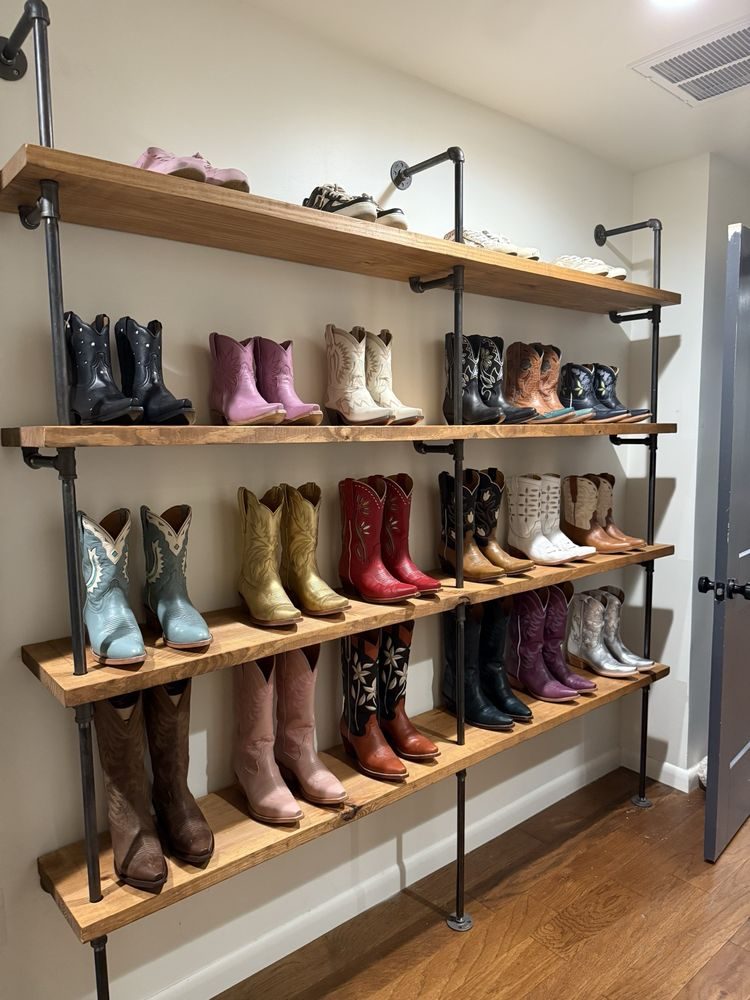 Floor-to-ceiling black pipe shelving full of cowboy boots