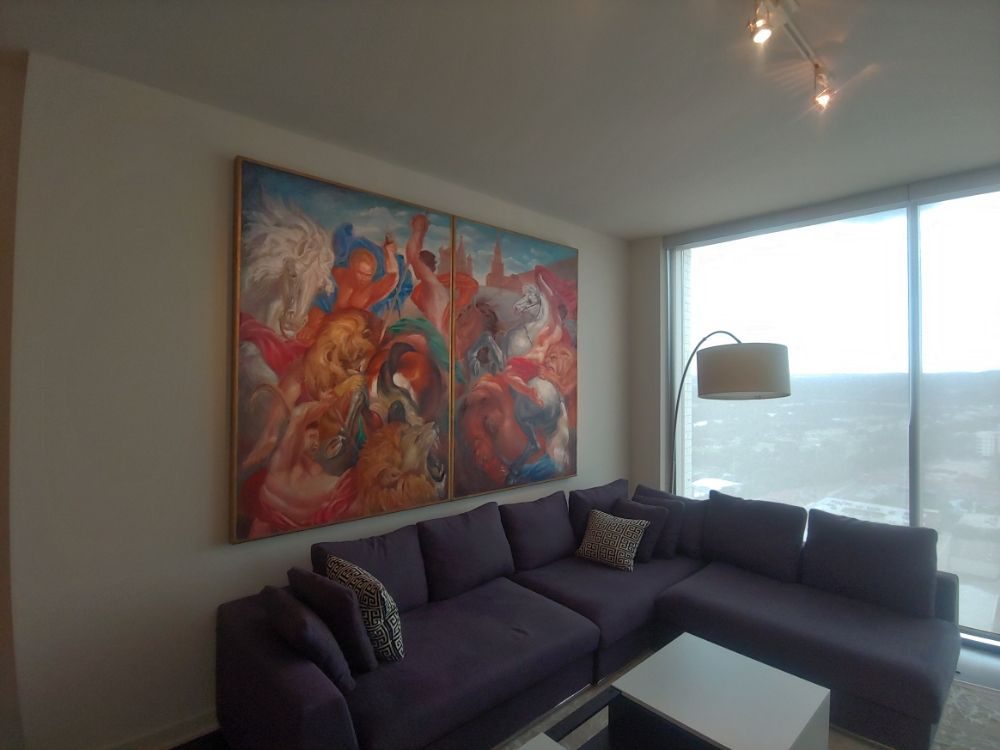 Large colorful painting hung above a sectional sofa by a bright window