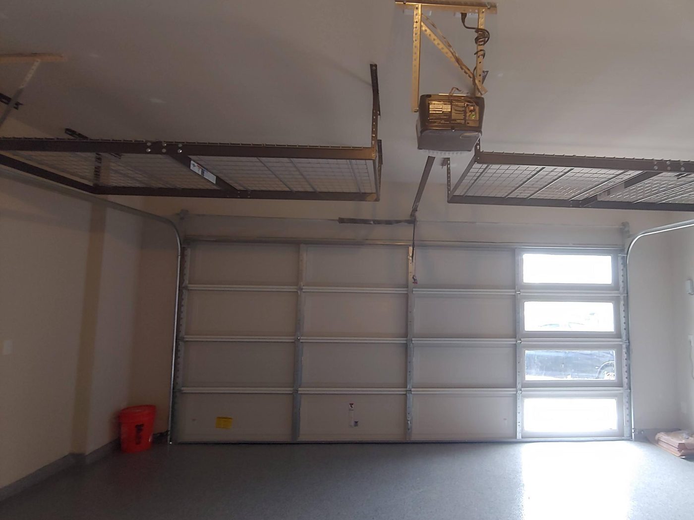 Two overhead wire storage racks hung on either side of the garage door opener, just above the garage door
