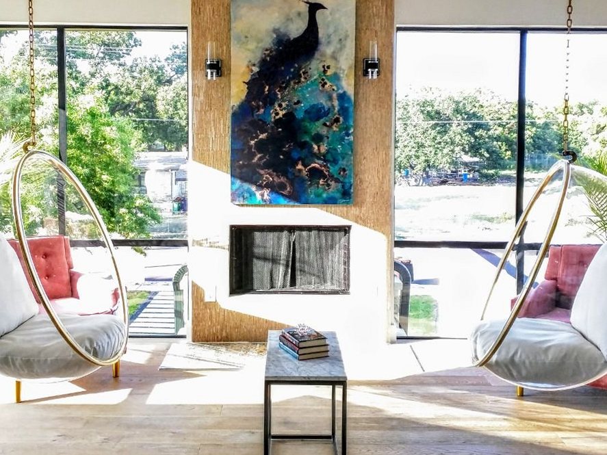 Two clear hanging pod chairs on either side of a fireplace and painting
